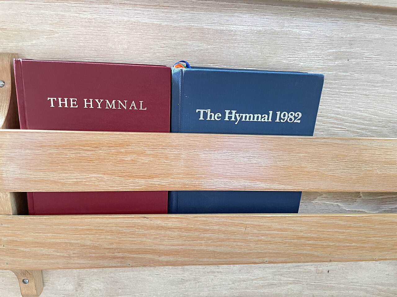 Två psalmböcker i hyllan på en kyrkbänk.