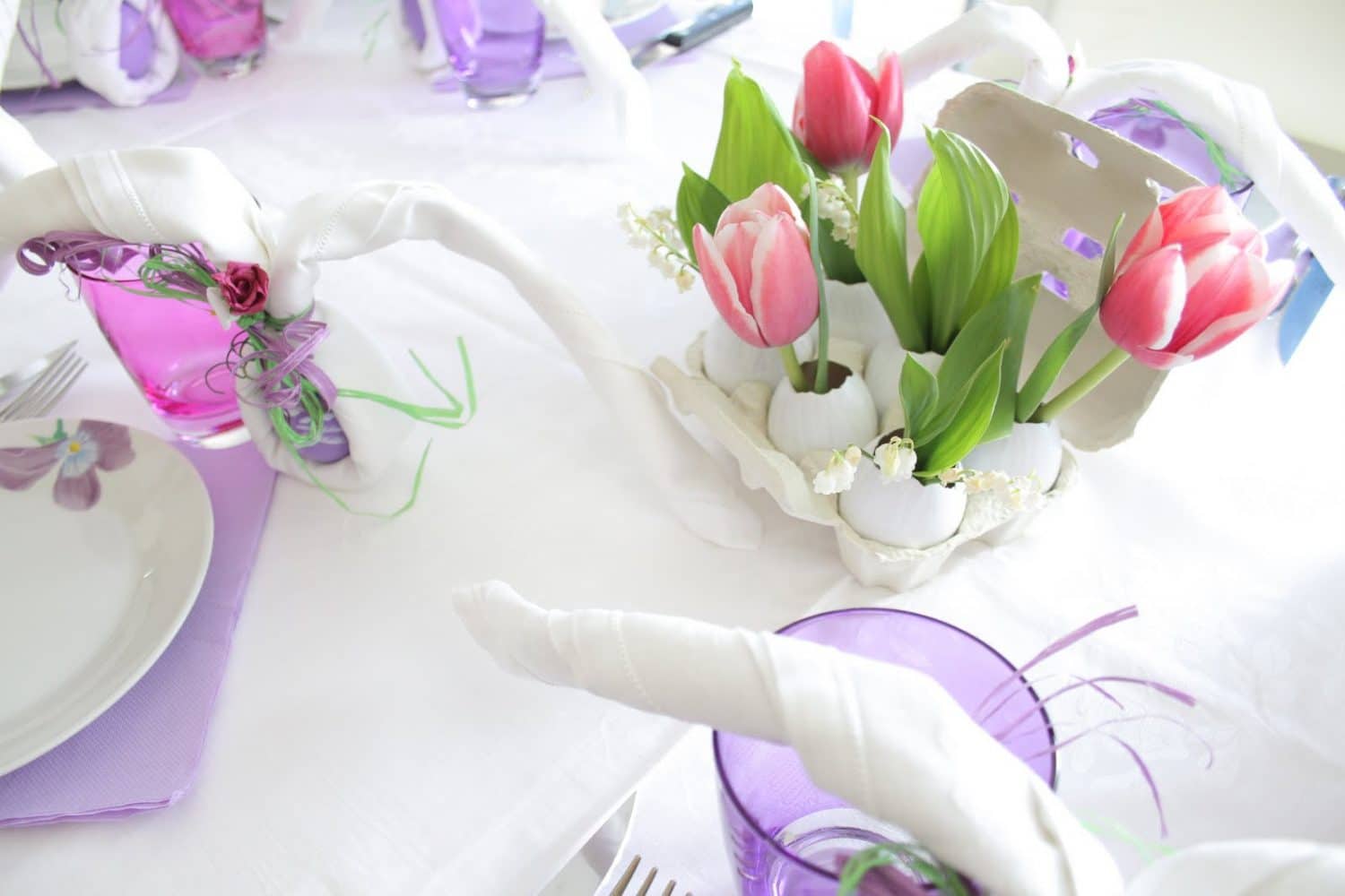 Festdukning med tulpaner, vita servetter och rosa glas.